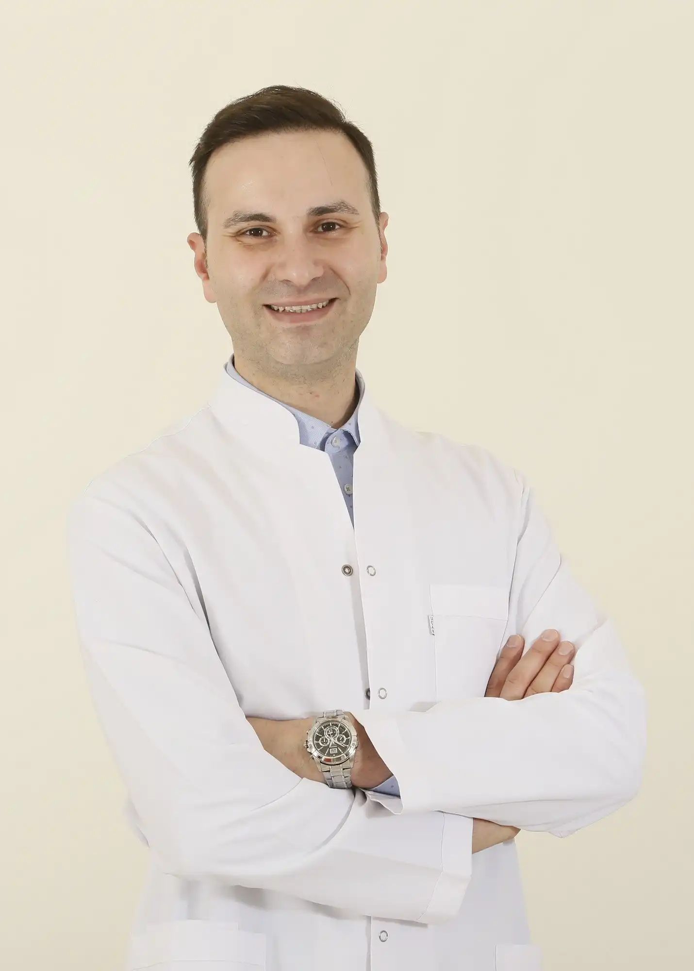 Dr. Burak Büyüktürk, beyaz önlüğüyle kollarını kavuşturmuş, gülümsüyor