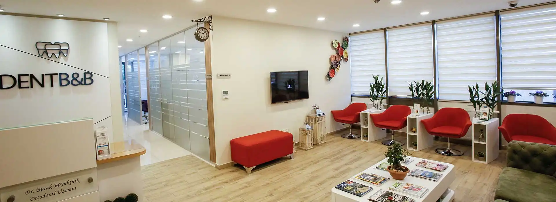 Dent BB kliniğinin bekleme alanı: gün ışığı alan geniş pencereler, kırmızı koltuklar ve resepsiyon